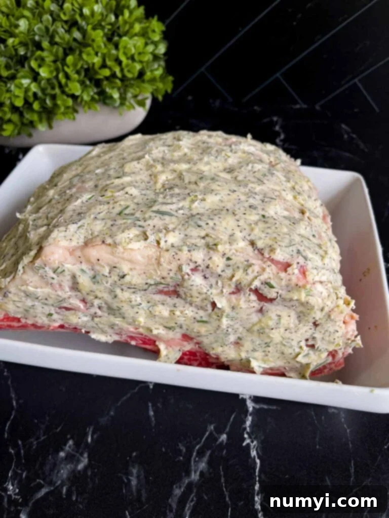 Closed Oven Prime Rib Roast 5 Uncooked bone-in prime rib roast coated with an herb butter compound, placed in a shallow roasting pan ready for the oven.