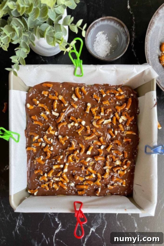 Salty Sweet Peanut Butter Pretzel Bars 9 Peanut butter pretzel bars in a parchment lined baking pan with toppings.
