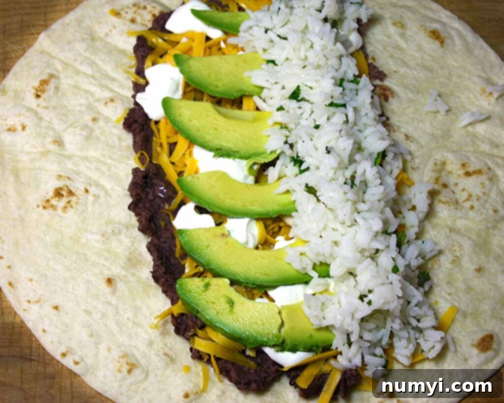 Vegetarian Burrito - An easy, meatless meal option! Fresh, tangy and absolutely delicious! A large flour tortilla is being assembled with an initial layer of refried beans, shredded cheese, and cilantro lime rice for a vegetarian burrito.