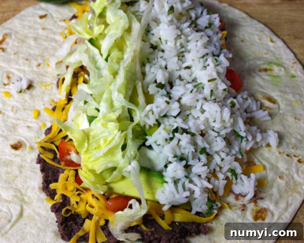 Vegetarian Burrito - An easy, meatless meal option! Fresh, tangy and absolutely delicious! A vegetarian burrito being assembled on a countertop, with a generous spread of ingredients including rice, beans, avocado, and lettuce, ready for rolling.