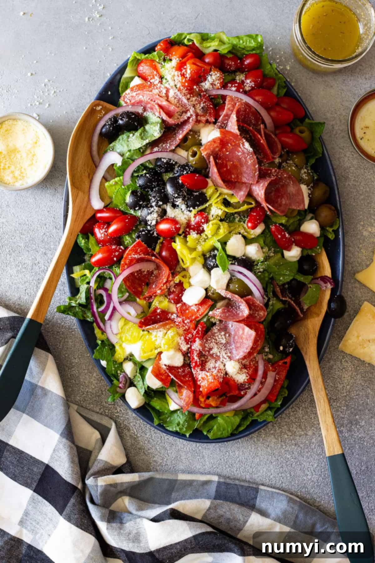 Big Italian Deli Salad 2 A large platter generously filled with colorful Antipasto Salad, featuring various Italian meats, cheeses, olives, and fresh vegetables, with serving spoons on the side.
