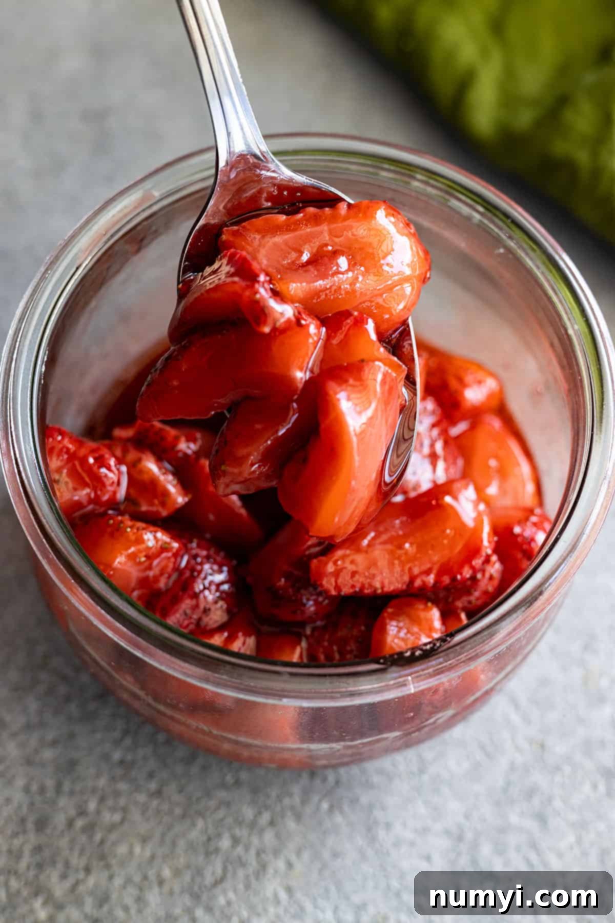 Roasted strawberries in a clear glass jar with a spoon, highlighting their glossy, syrupy texture, ready to be served or stored.