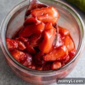 Roasted strawberries in a glass jar with a spoon pulling up a spoonful of glossy strawberries.