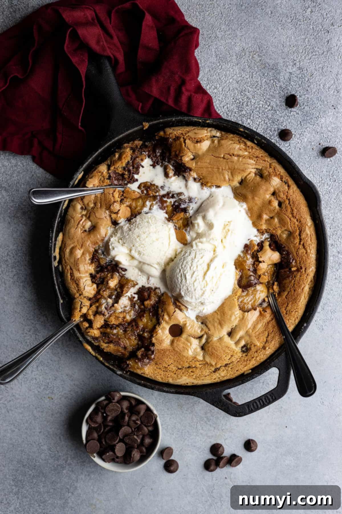 Overhead view of skillet cookie with spoons digging in and ice cream melting on top.
