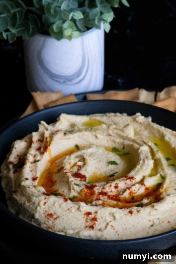 Creamy homemade hummus in a black bowl with a spoon, surrounded by fresh herbs and pita bread.