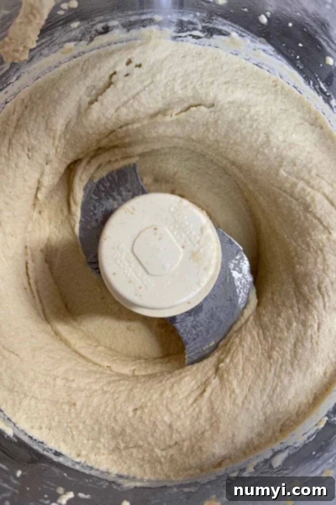 Pureed, smooth, and creamy hummus in the bowl of a food processor, ready to be transferred.