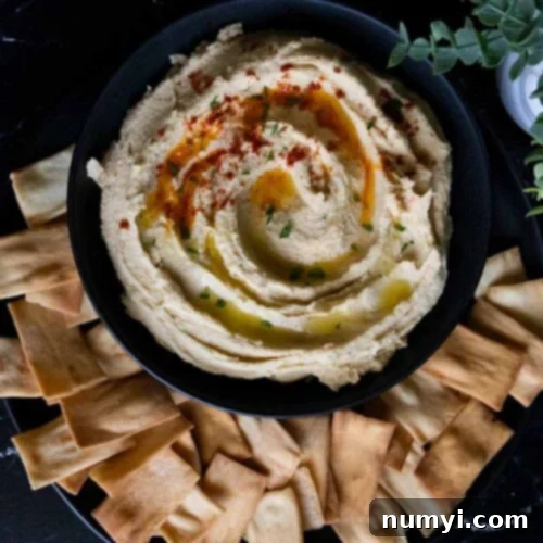 Homemade hummus in a black bowl surrounded by pita chips.