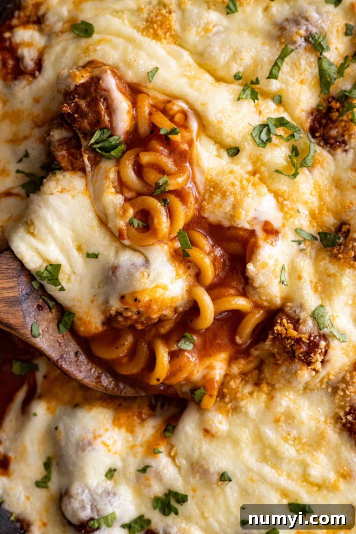 Close up of cheesy spaghettios with meatballs with a spoon in it. 