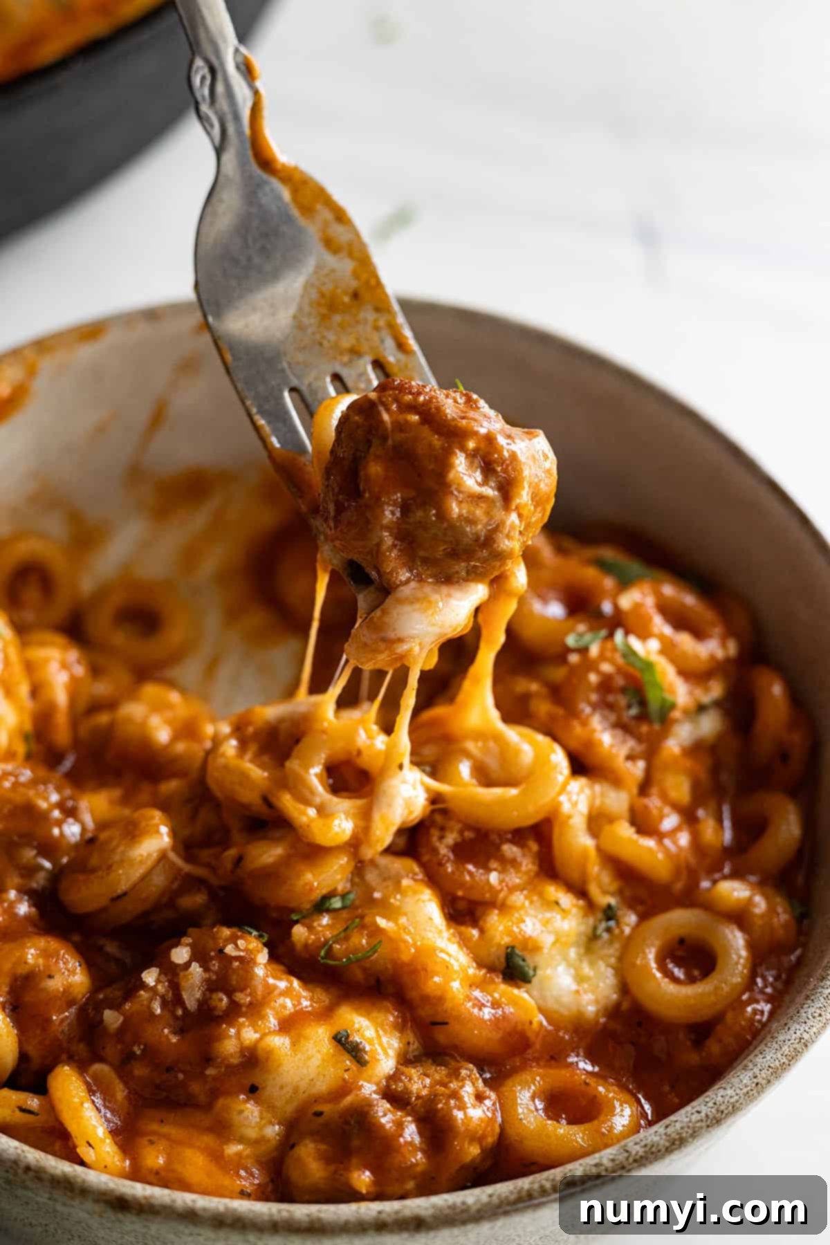 A meatball on a fork being pulled up from the bowl of spaghettios. 