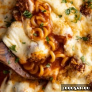 Close up of cheesy spaghettios with meatballs with a spoon in it.