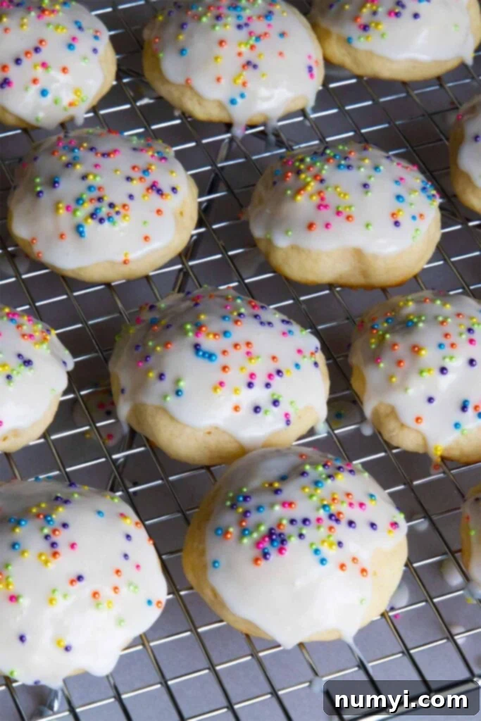 Stack of four glazed Italian ricotta cookies on a white plate, with a background of more cookies