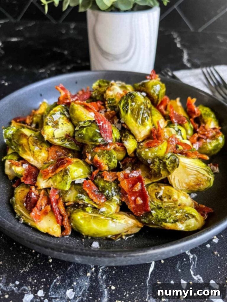 A plate of perfectly roasted brussels sprouts with honey butter and crispy bacon, garnished.