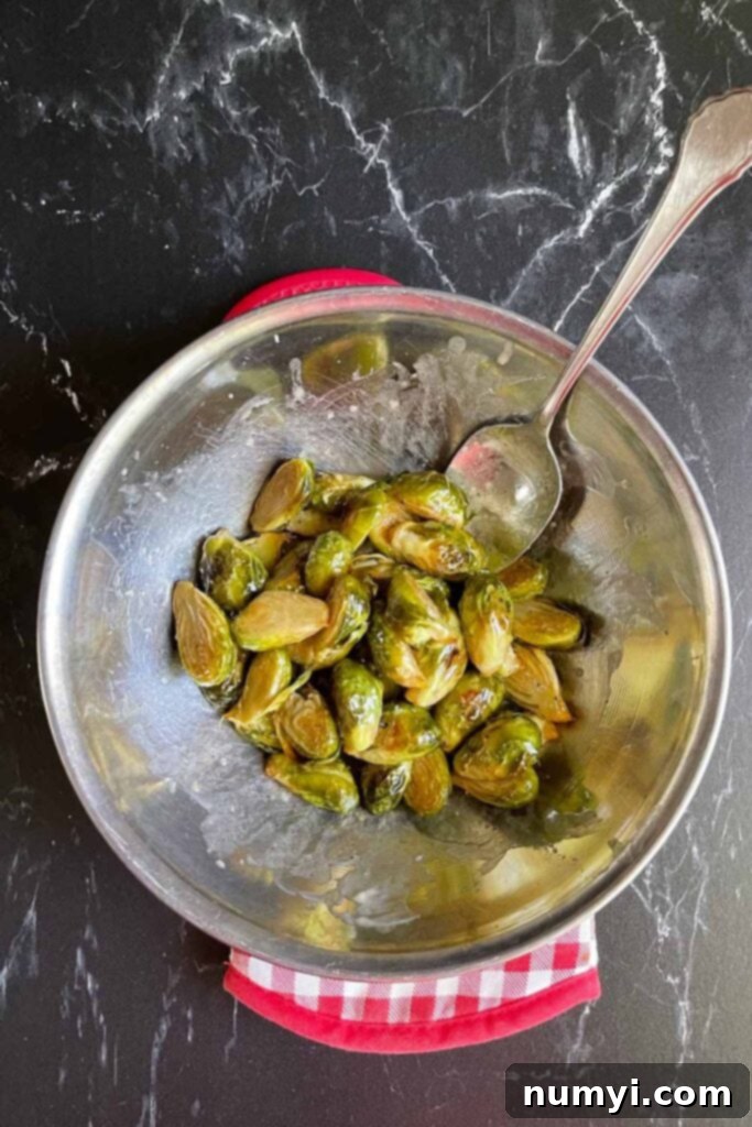 Roasted brussels sprouts being tossed with honey butter in a bowl.