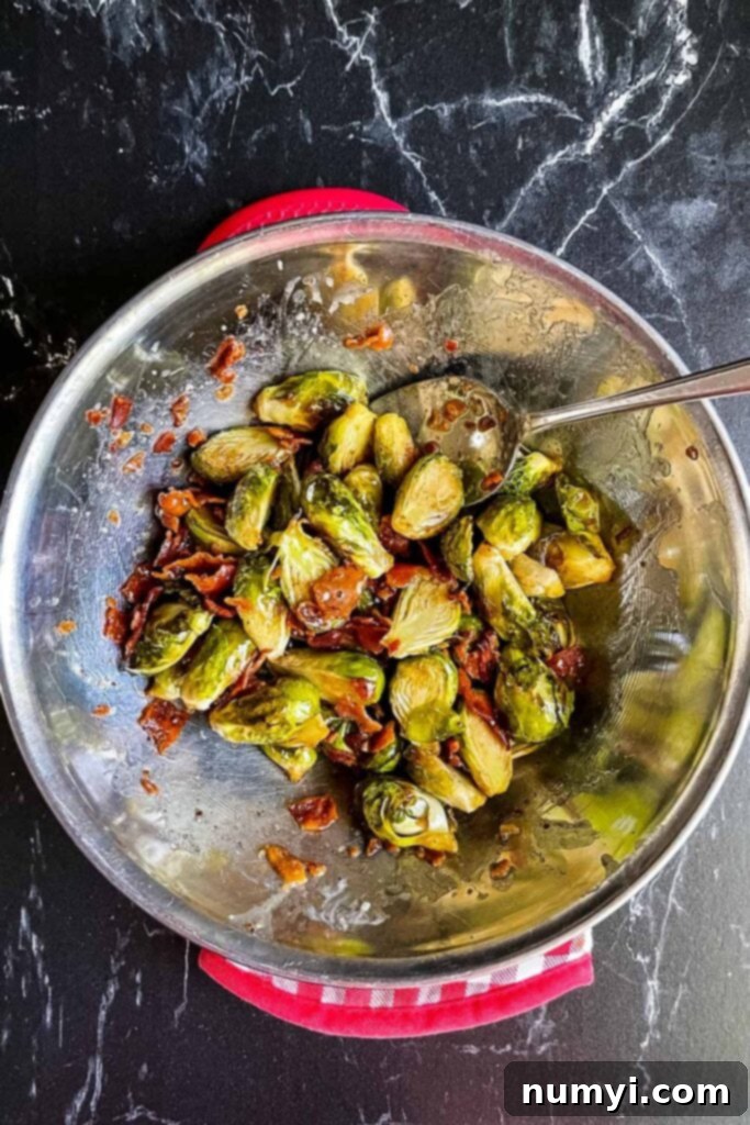 Roasted brussels sprouts with honey butter and crumbled bacon in a stainless steel bowl, ready to mix.