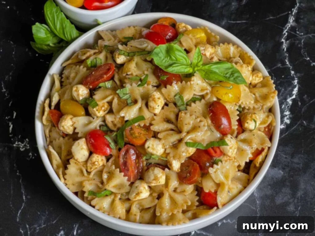 Pesto pasta Caprese salad in a white bowl, garnished with fresh basil.