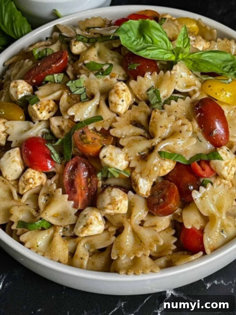 Close-up of vibrant Caprese pasta salad in a white bowl, showing pasta, mozzarella pearls, and halved tomatoes.