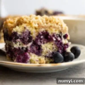 Blueberry buckle on a plate with blueberries off to the side.