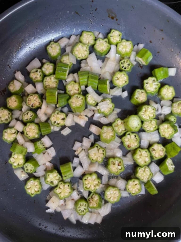 Diced sweet onions and fresh okra sautéing in bacon fat in a large skillet, forming the flavor base for the succotash.