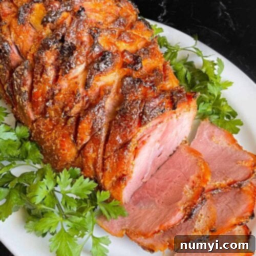A beautifully cooked brown sugar glazed ham, sliced and arranged on a platter, garnished with fresh parsley.