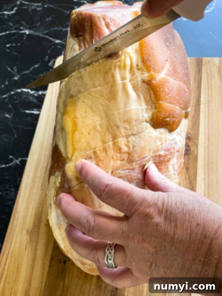 A close-up shot showing diagonal cuts being carefully made into the fat cap of a ham using a sharp knife.