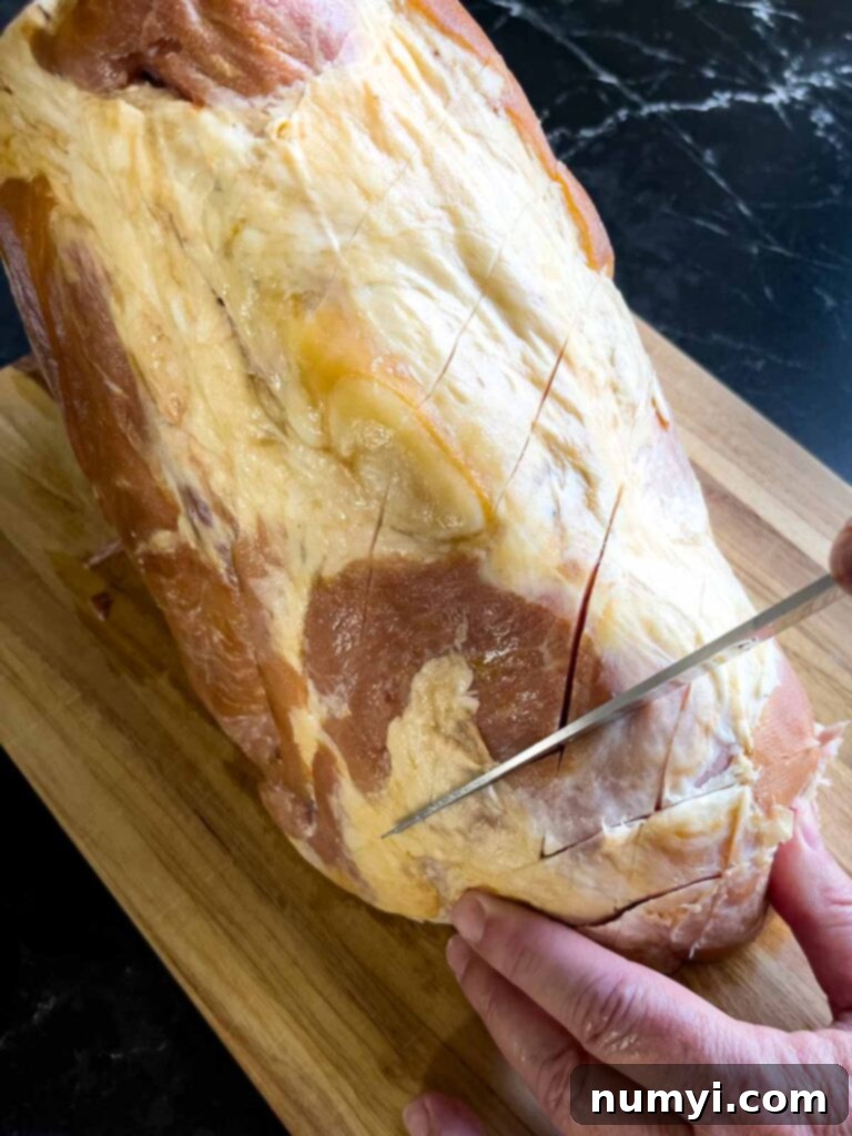 A ham with diagonal cuts in opposite directions, forming a diamond pattern across its surface, ready for glazing.