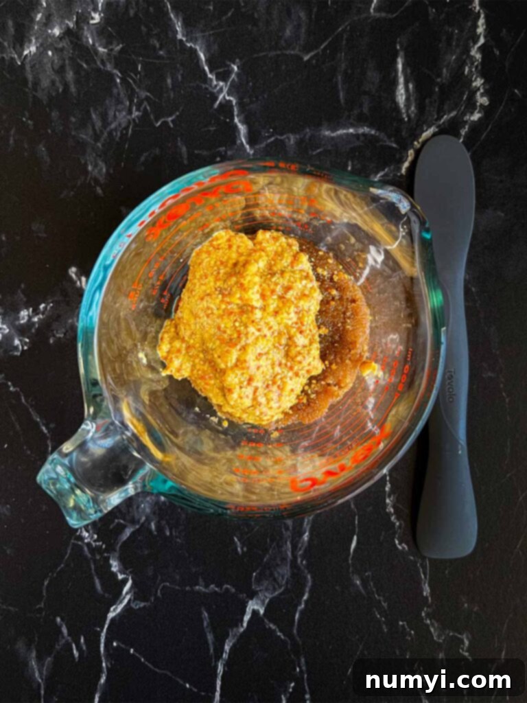 A glass measuring cup holding the combined brown sugar glaze ingredients: dark brown sugar, whole grain mustard, and apple cider vinegar.