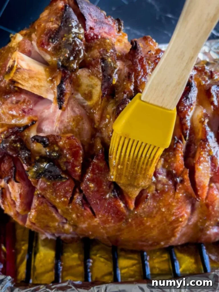 A chef's hand brushing a thick, glossy brown sugar glaze evenly over the surface of a partially baked ham.