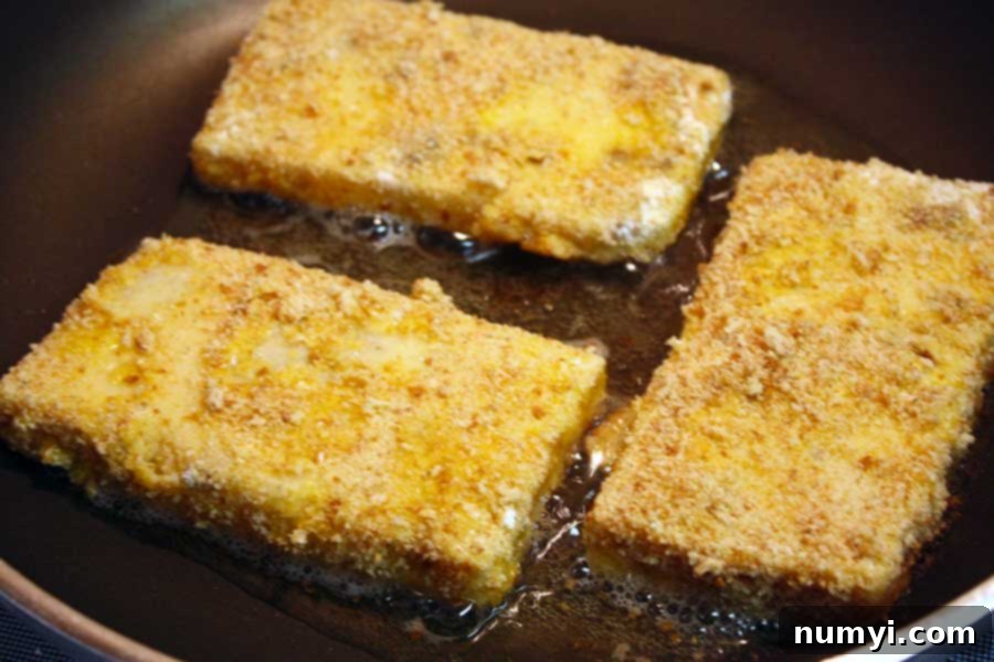 Fried Grit Cakes in a hot frying pan, showcasing the golden-brown crisping process as they cook.
