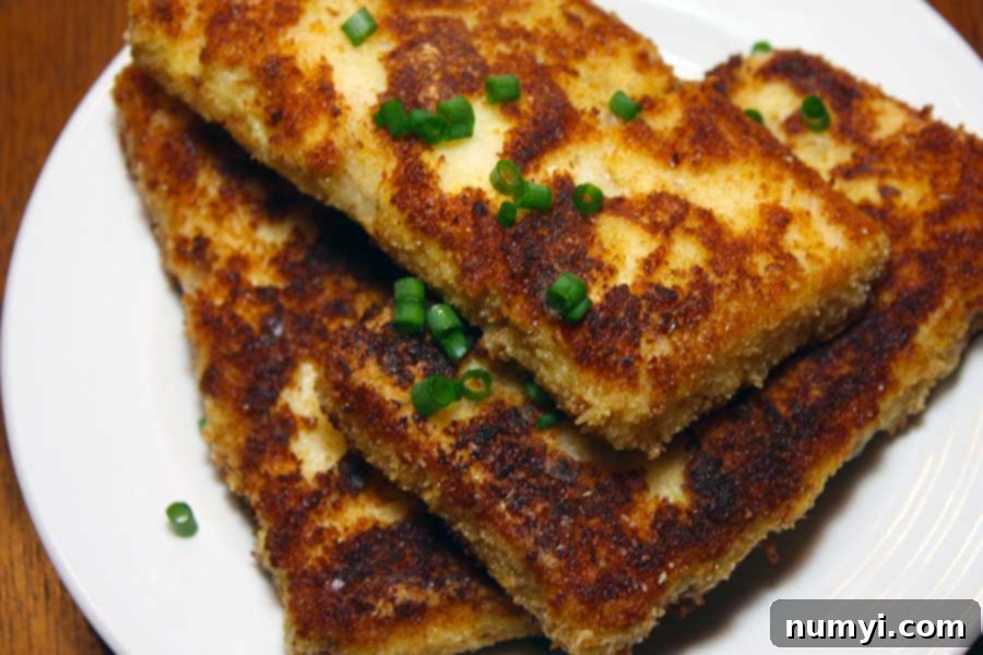 Two perfectly fried grit cakes on a white plate, beautifully garnished with diced green onions, highlighting their golden crust.