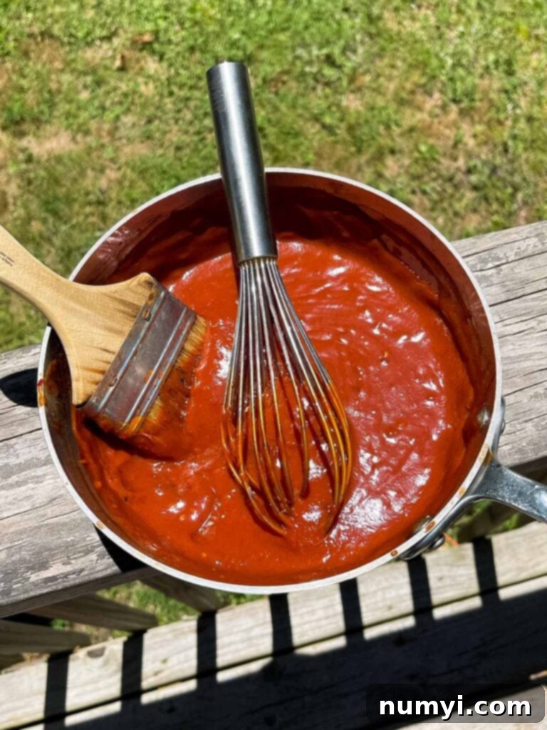 Smoky Bourbon Chipotle BBQ Sauce 3 Homemade bourbon chipotle BBQ sauce simmering in a saucepan on a rustic deck rail, ready for tasting.