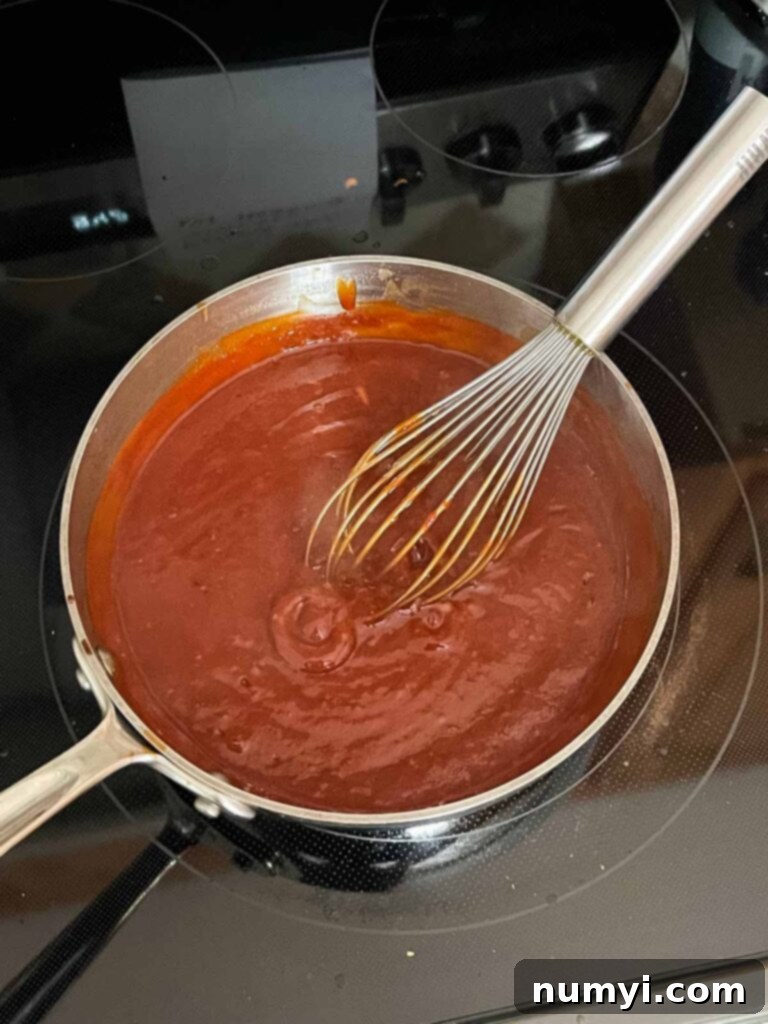Smoky Bourbon Chipotle BBQ Sauce 5 The homemade BBQ sauce bubbling gently in a saucepan on the stovetop, thickening to perfection.