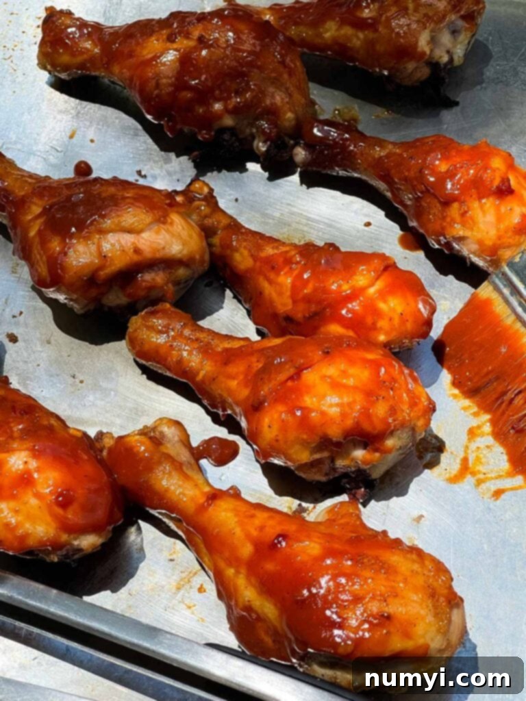 Applying rich barbecue sauce to grilled chicken legs on the grill.