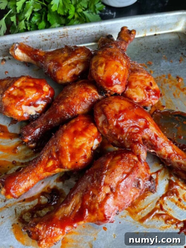 Close-up of BBQ chicken legs on a baking sheet, showcasing crispy skin.