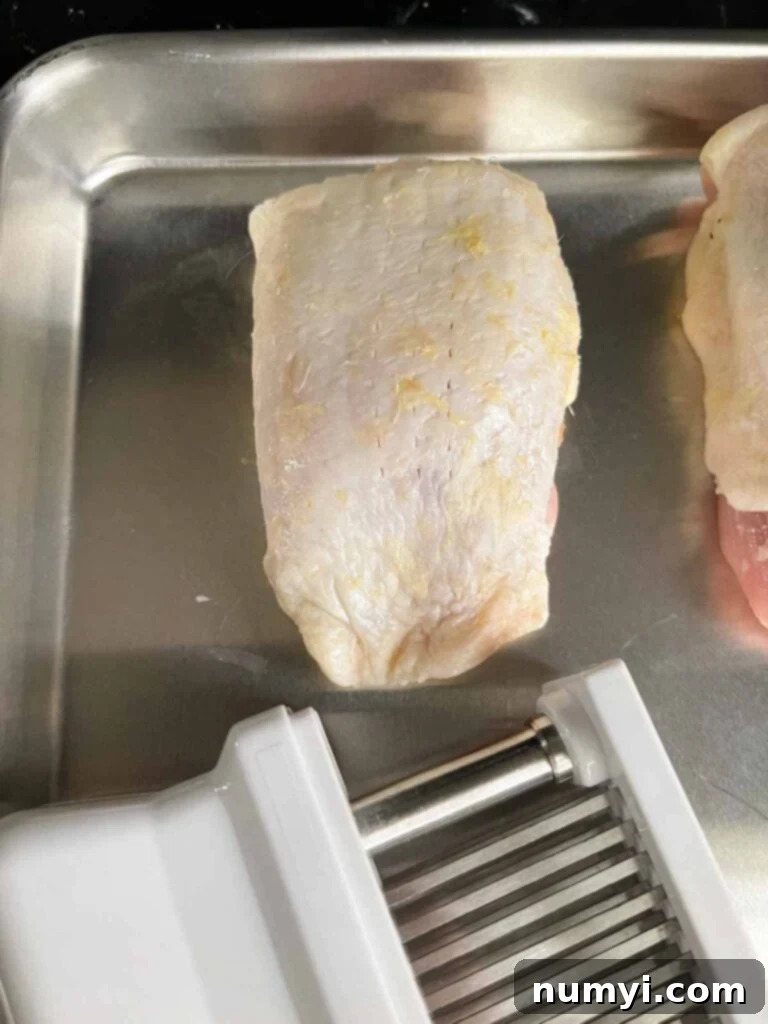 raw chicken thigh showing pierced skin from a meat tenderizer.