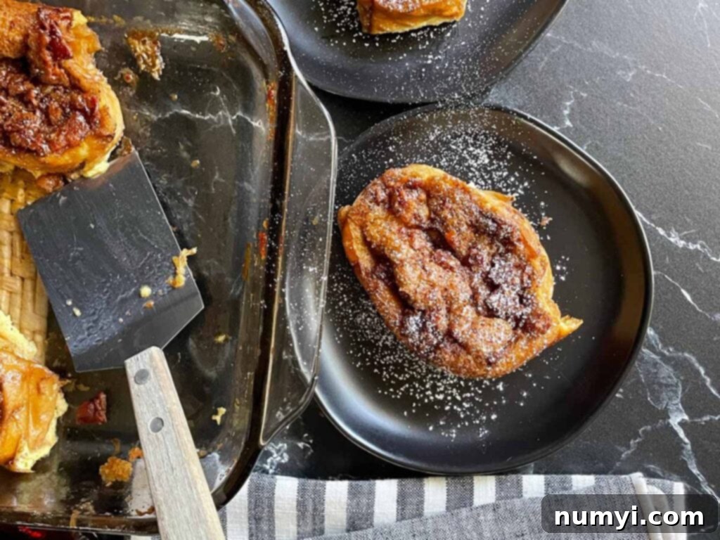 Slices of overnight maple bacon baked french toast on black plates garnished with powdered sugar.