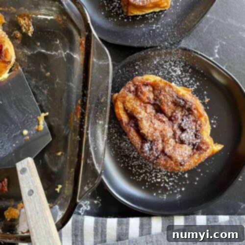 Slices of overnight maple bacon baked french toast on black plates garnished with powdered sugar.
