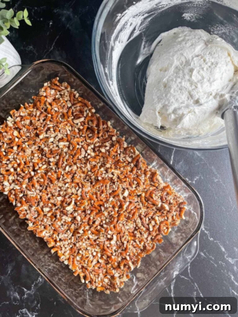 Pretzel crust in a 9x13 baking dish with a bowl of a whipped cream filling next to it.