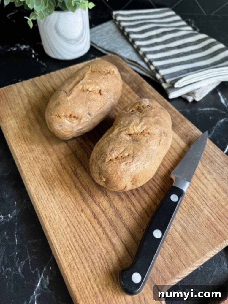 Two baked russet potatoes on a cutting board, ready for preparation.
