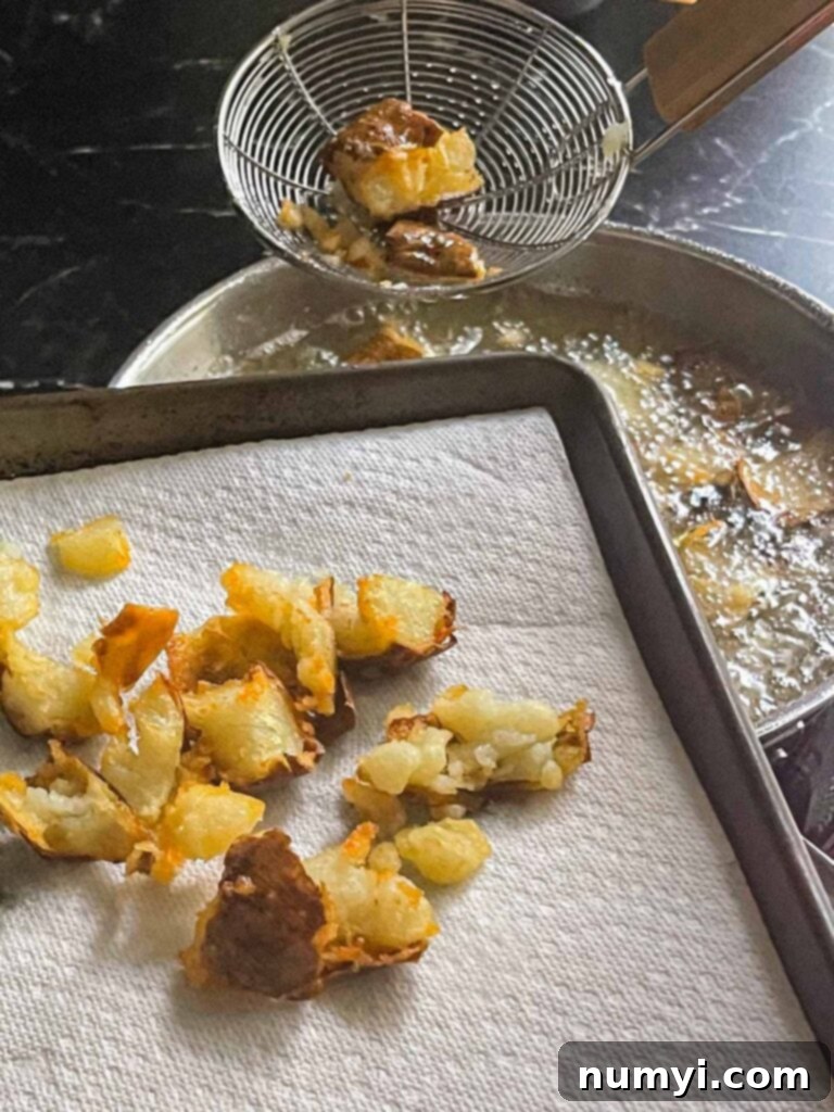Fried potato pieces being removed from hot oil with a slotted spoon to drain.