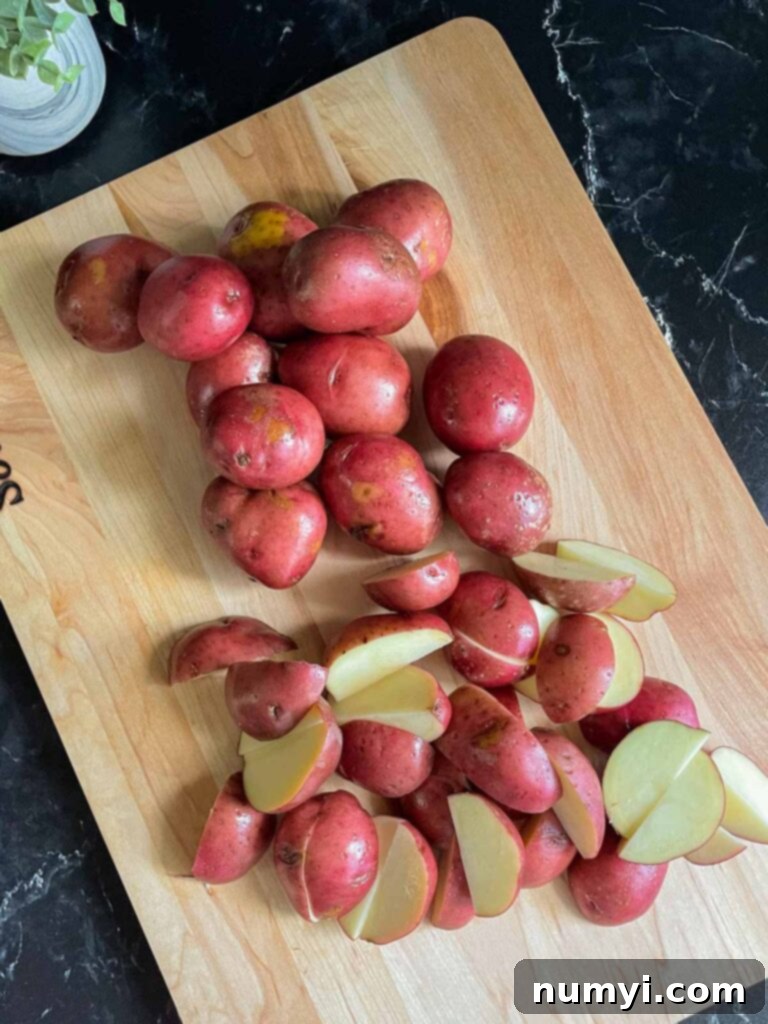 Cleaned and quartered baby red potatoes arranged on a wooden cutting board, ready for cooking.