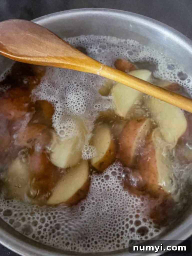 Red potatoes boiling in a large pot on the stovetop, covered with water.