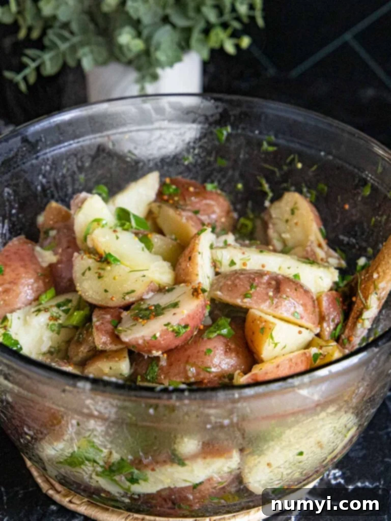 Warm, dressed herb potato salad with green onions in a clear glass bowl, ready for serving.