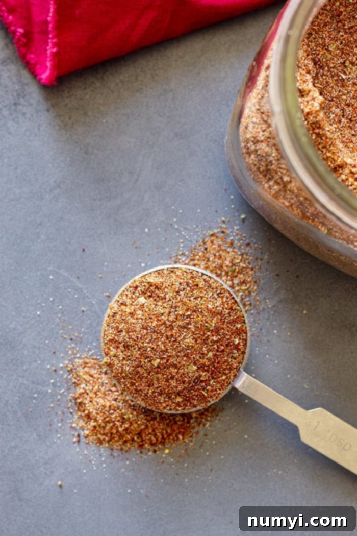 A measuring spoon filled with homemade taco seasoning, showing the rich color and texture of the blend.