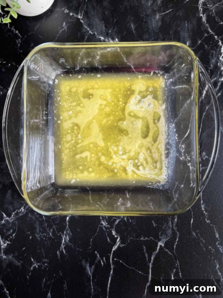 Effortless Butter Swim Biscuits 6 A square glass baking dish holding a shimmering pool of freshly melted butter, ready for the biscuit dough.
