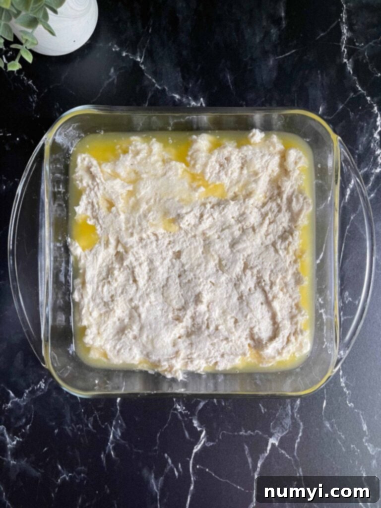 Effortless Butter Swim Biscuits 7 Biscuit dough perfectly spread and evenly distributed into a baking pan filled with melted butter, ready for scoring.