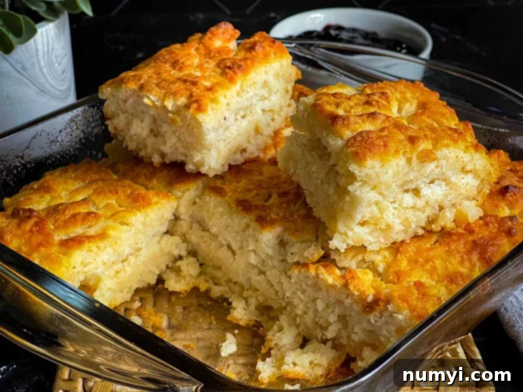 Effortless Butter Swim Biscuits 9 Two perfectly baked butter swim biscuits resting on top of the pan, which contains the remaining biscuits already cut into squares, showcasing their golden-brown crust.