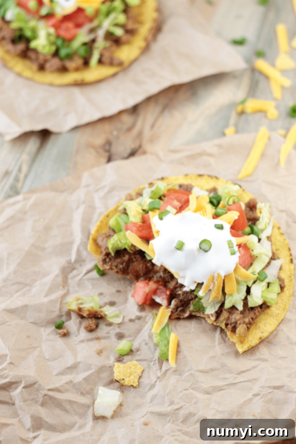 a beef and bean tostada with bites taken out o it on a piece of parchment paper
