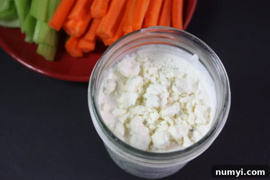 Freshly made blue cheese dressing in a mason jar, with crisp carrots and celery sticks ready for dipping in the background.