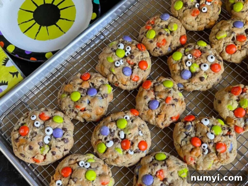 Halloween monster cookies arranged neatly on a wire cooling rack set inside a baking sheet, showcasing their vibrant colors and candy eyeballs.