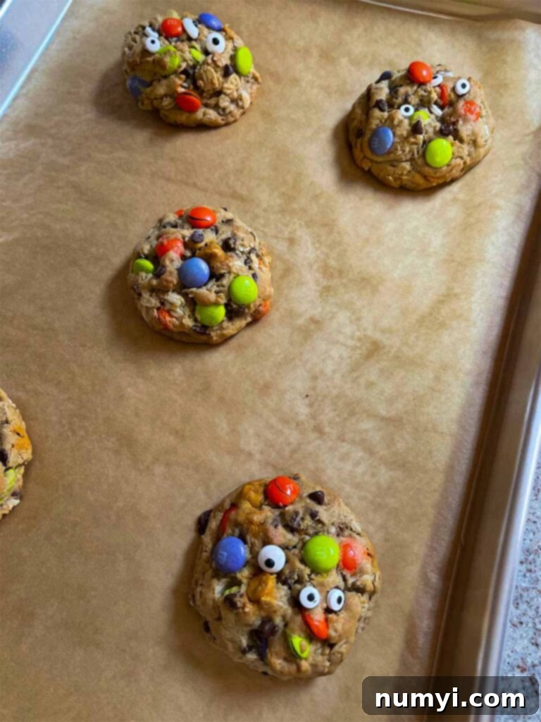 Freshly baked Halloween monster cookies with candy eyes, cooling on a parchment-lined baking sheet.